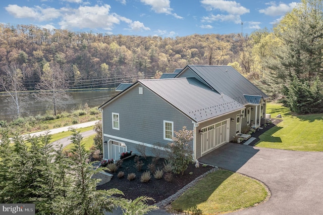 view of side of home with a yard, a standing seam roof, metal roof, a wooded view, and driveway