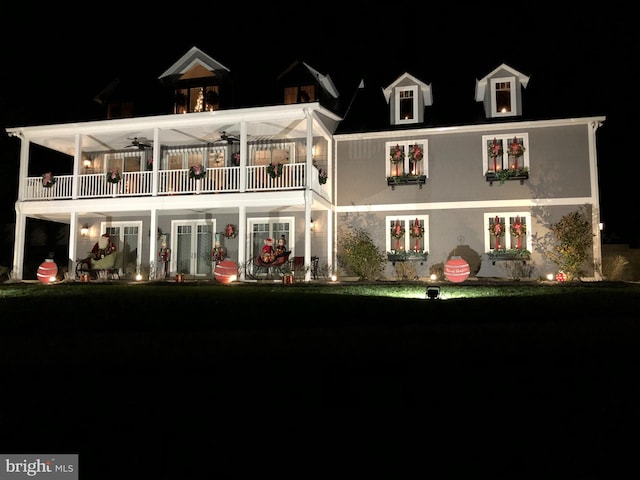 back of house at night with ceiling fan and a balcony