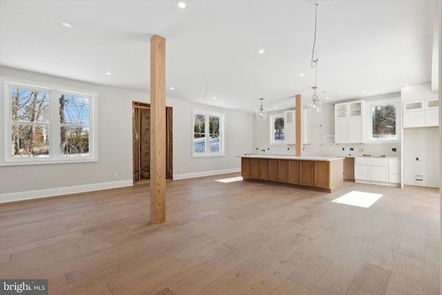 kitchen with a large island, hanging light fixtures, glass insert cabinets, open floor plan, and white cabinets