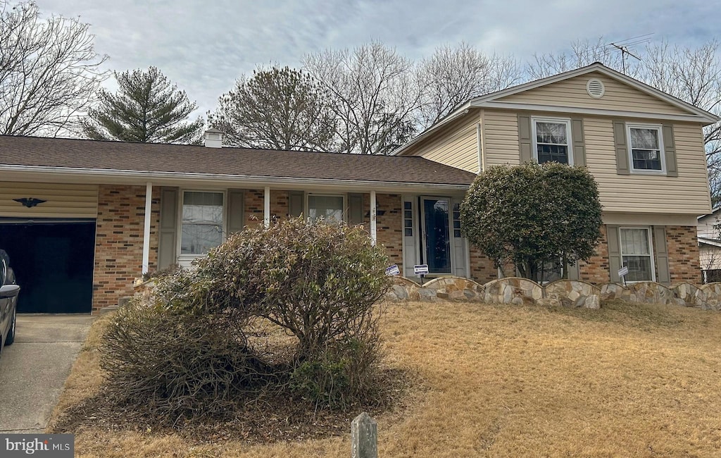 tri-level home with a garage, a chimney, a front lawn, and brick siding