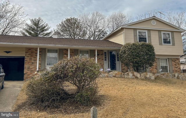 tri-level home with a garage, a chimney, a front lawn, and brick siding