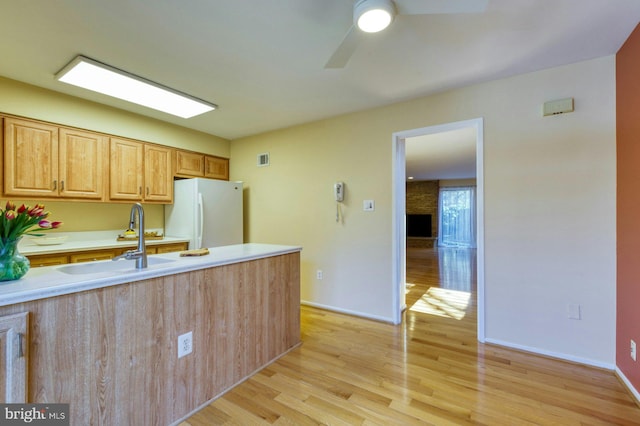 kitchen featuring freestanding refrigerator, ceiling fan, a sink, light countertops, and light wood-type flooring