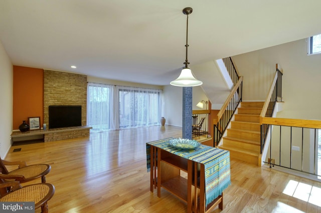 living room featuring recessed lighting, light wood-style flooring, a brick fireplace, and stairs