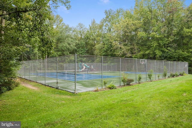 view of tennis court with a lawn and fence