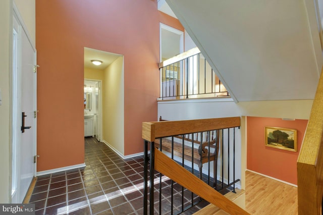 corridor featuring baseboards, an upstairs landing, and vaulted ceiling