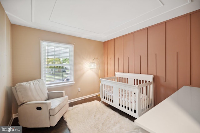 bedroom with a crib, dark wood finished floors, and baseboards