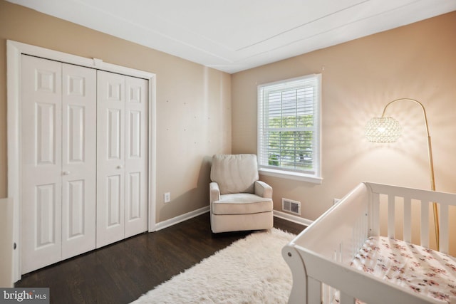 bedroom featuring visible vents, baseboards, a closet, a nursery area, and dark wood-style floors