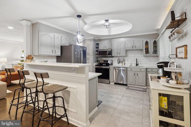 kitchen with a breakfast bar, pendant lighting, light countertops, appliances with stainless steel finishes, and glass insert cabinets