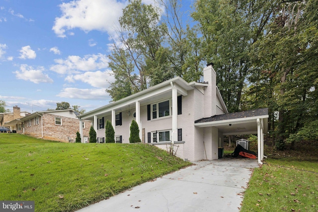 view of front facade featuring brick siding, a chimney, an attached carport, driveway, and a front lawn