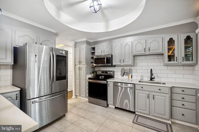 kitchen with glass insert cabinets, appliances with stainless steel finishes, a tray ceiling, light countertops, and a sink