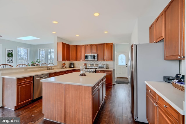 kitchen featuring a center island, appliances with stainless steel finishes, a skylight, dark wood-style floors, and a sink