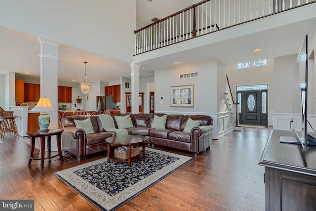 living area featuring visible vents, a wainscoted wall, dark wood-type flooring, a high ceiling, and ornate columns