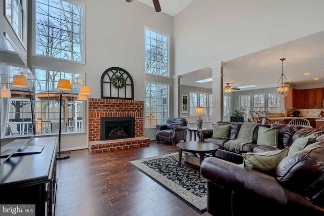 living room featuring a fireplace, dark wood-type flooring, ceiling fan, and decorative columns