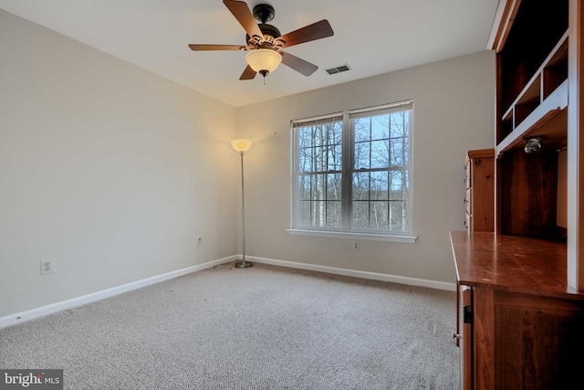 carpeted empty room featuring visible vents, a ceiling fan, and baseboards