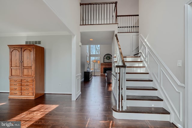 staircase with visible vents, ornamental molding, wood finished floors, a high ceiling, and baseboards