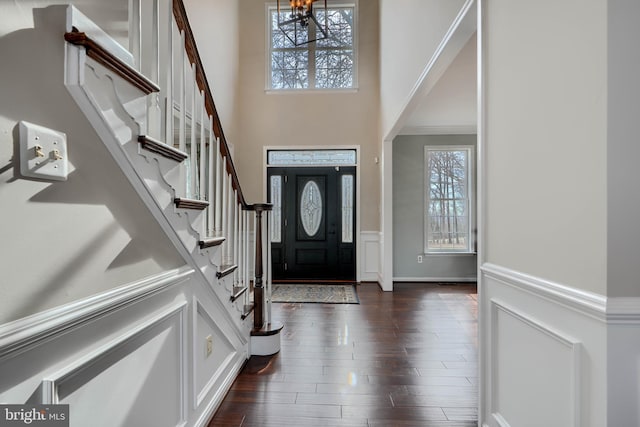 entryway with stairway, wainscoting, a towering ceiling, and dark wood-style flooring