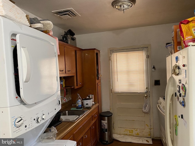 kitchen featuring white appliances, visible vents, a sink, stacked washer and dryer, and brown cabinets