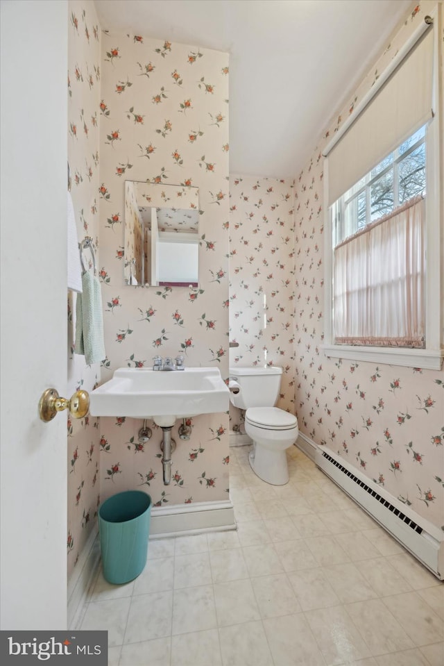 half bathroom with a baseboard radiator, baseboards, toilet, and wallpapered walls