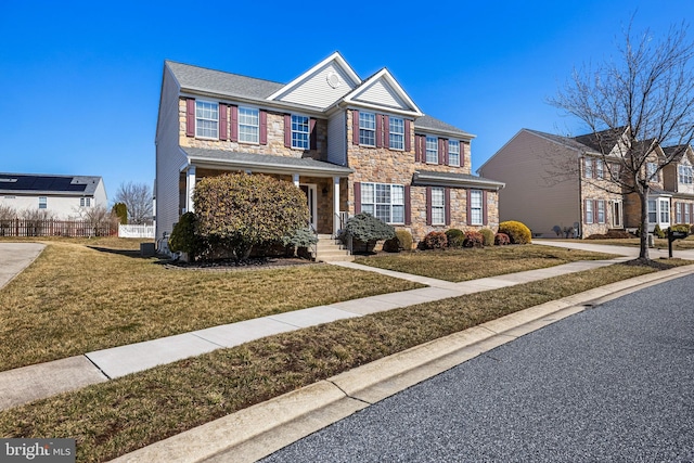 traditional-style home featuring stone siding, fence, and a front lawn