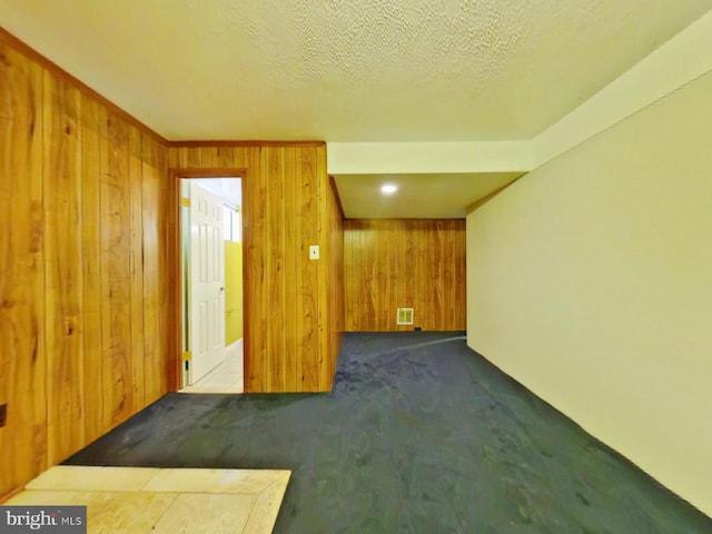 empty room featuring wood walls, visible vents, dark colored carpet, and a textured ceiling