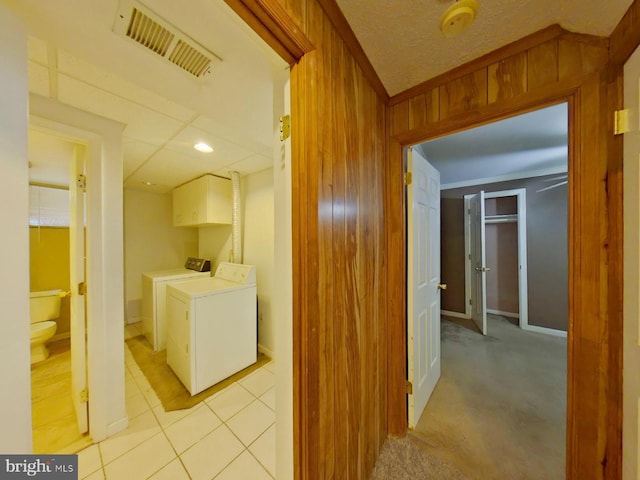 hallway featuring washing machine and dryer, wooden walls, visible vents, and light tile patterned flooring