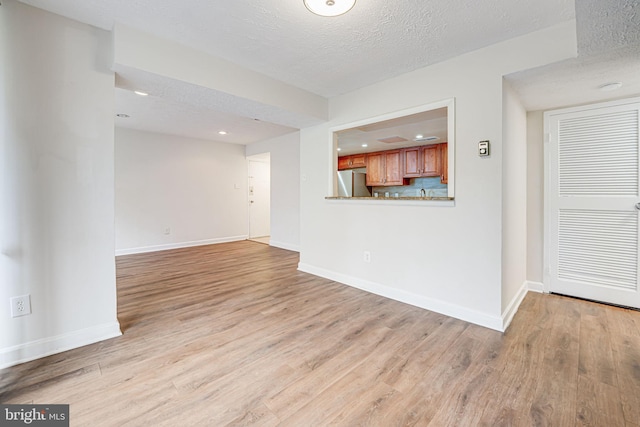 unfurnished living room featuring recessed lighting, baseboards, a textured ceiling, and light wood finished floors