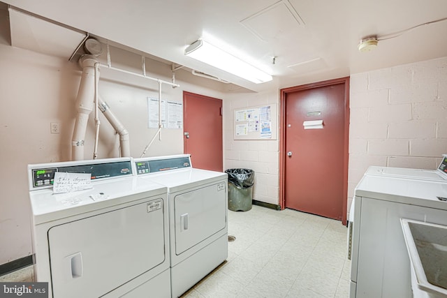 community laundry room with light floors, independent washer and dryer, and concrete block wall