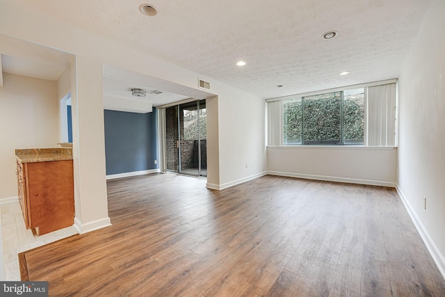 spare room with baseboards, a textured ceiling, visible vents, and wood finished floors