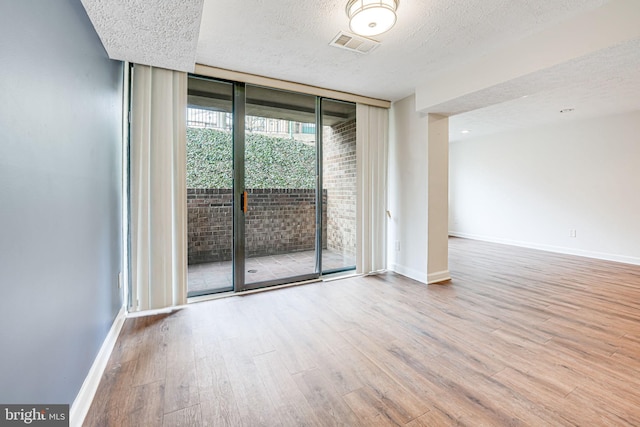 empty room with a textured ceiling, a wall of windows, wood finished floors, and baseboards