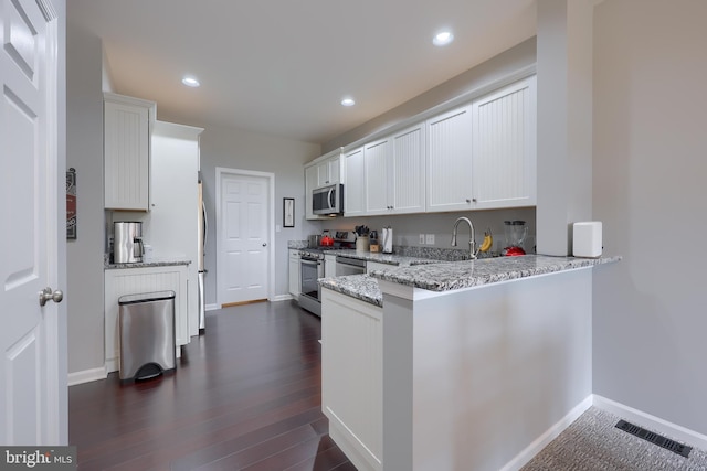 kitchen with stainless steel appliances, a peninsula, white cabinetry, visible vents, and light stone countertops