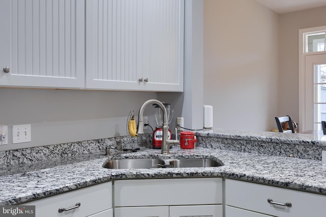 kitchen with light stone counters, a sink, and white cabinetry