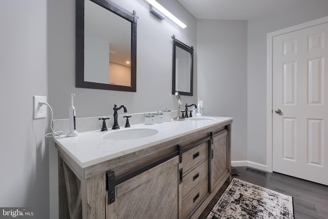 full bathroom with double vanity, a sink, baseboards, and wood finished floors