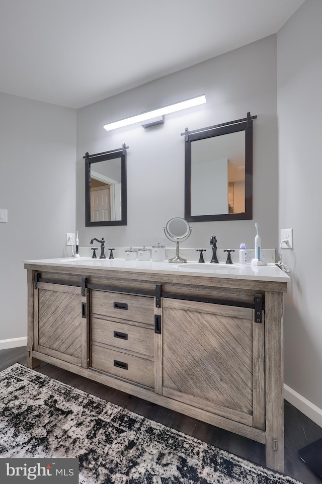 bathroom with double vanity, baseboards, a sink, and wood finished floors