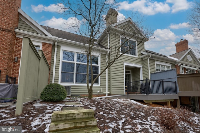 snow covered rear of property featuring a chimney and a deck