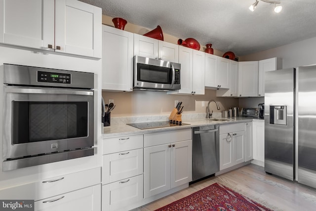 kitchen featuring a textured ceiling, appliances with stainless steel finishes, a sink, and white cabinetry