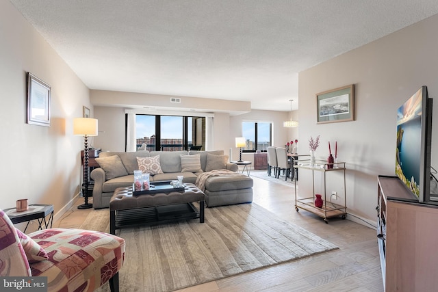 living room featuring a textured ceiling, light wood finished floors, visible vents, and baseboards