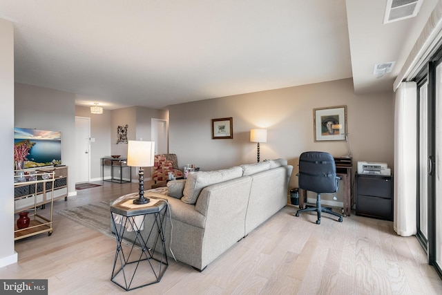 living area with light wood finished floors, visible vents, and baseboards