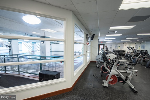 exercise room featuring a paneled ceiling, a healthy amount of sunlight, visible vents, and baseboards