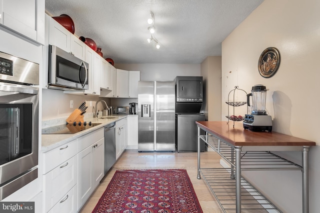 kitchen featuring a textured ceiling, light wood-style flooring, a sink, white cabinets, and appliances with stainless steel finishes