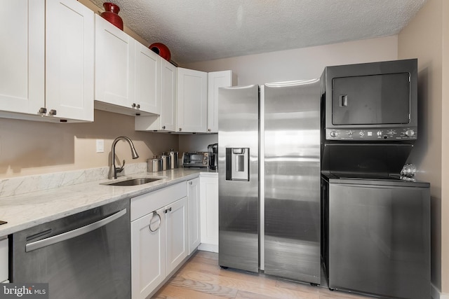 kitchen with light stone counters, appliances with stainless steel finishes, white cabinets, a sink, and stacked washing maching and dryer