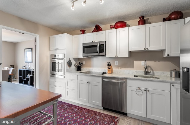 kitchen featuring appliances with stainless steel finishes, light stone countertops, a textured ceiling, white cabinetry, and a sink