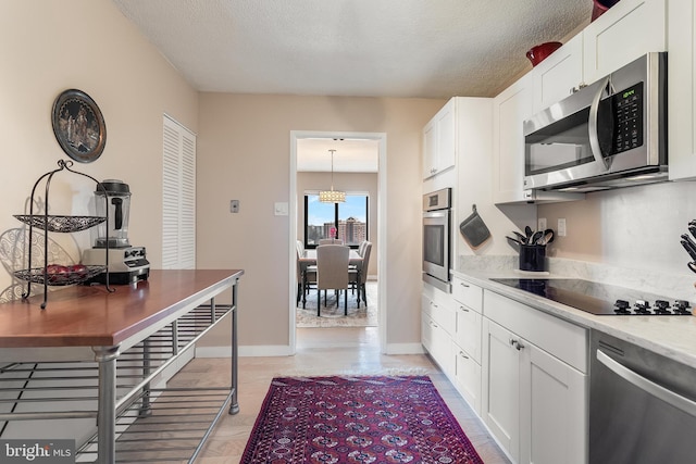 kitchen featuring appliances with stainless steel finishes, white cabinets, hanging light fixtures, and a textured ceiling