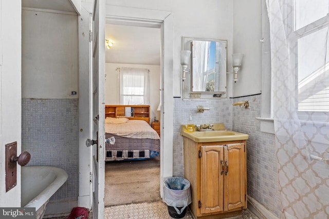 bathroom with ensuite bathroom, a bathing tub, vanity, tile walls, and wainscoting