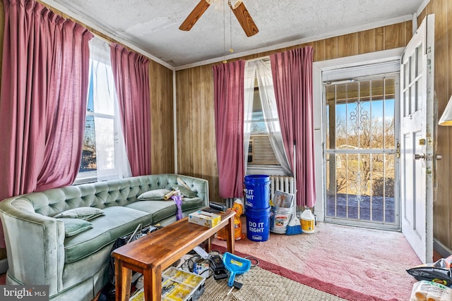 living area with carpet floors, wood walls, a textured ceiling, and ceiling fan