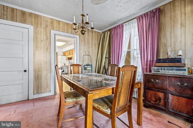 dining room featuring a chandelier, a textured ceiling, wooden walls, carpet floors, and ornamental molding