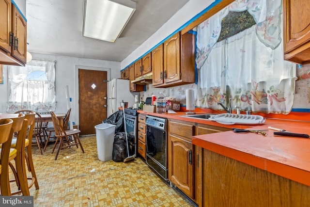 kitchen featuring dishwasher, brown cabinets, freestanding refrigerator, under cabinet range hood, and a sink