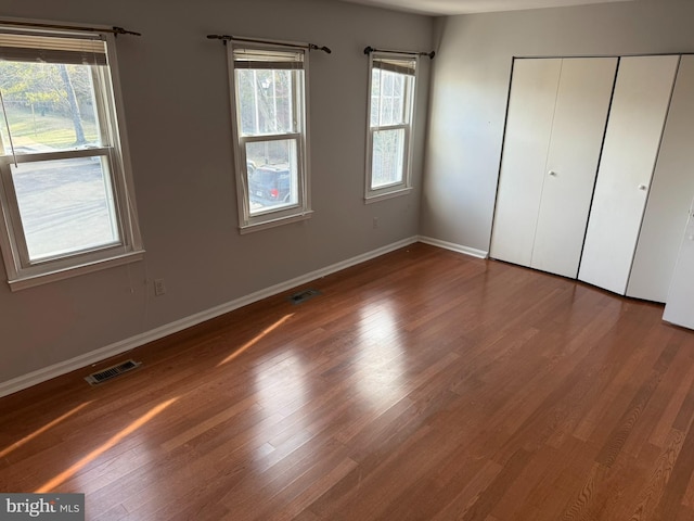 unfurnished bedroom featuring a closet, visible vents, baseboards, and wood finished floors