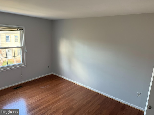 spare room featuring wood finished floors, visible vents, and baseboards