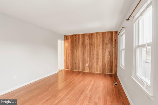 unfurnished room with visible vents, baseboards, light wood-style floors, and wooden walls