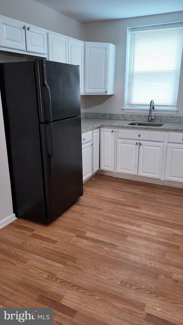 kitchen with light wood-style floors, freestanding refrigerator, white cabinetry, and a sink